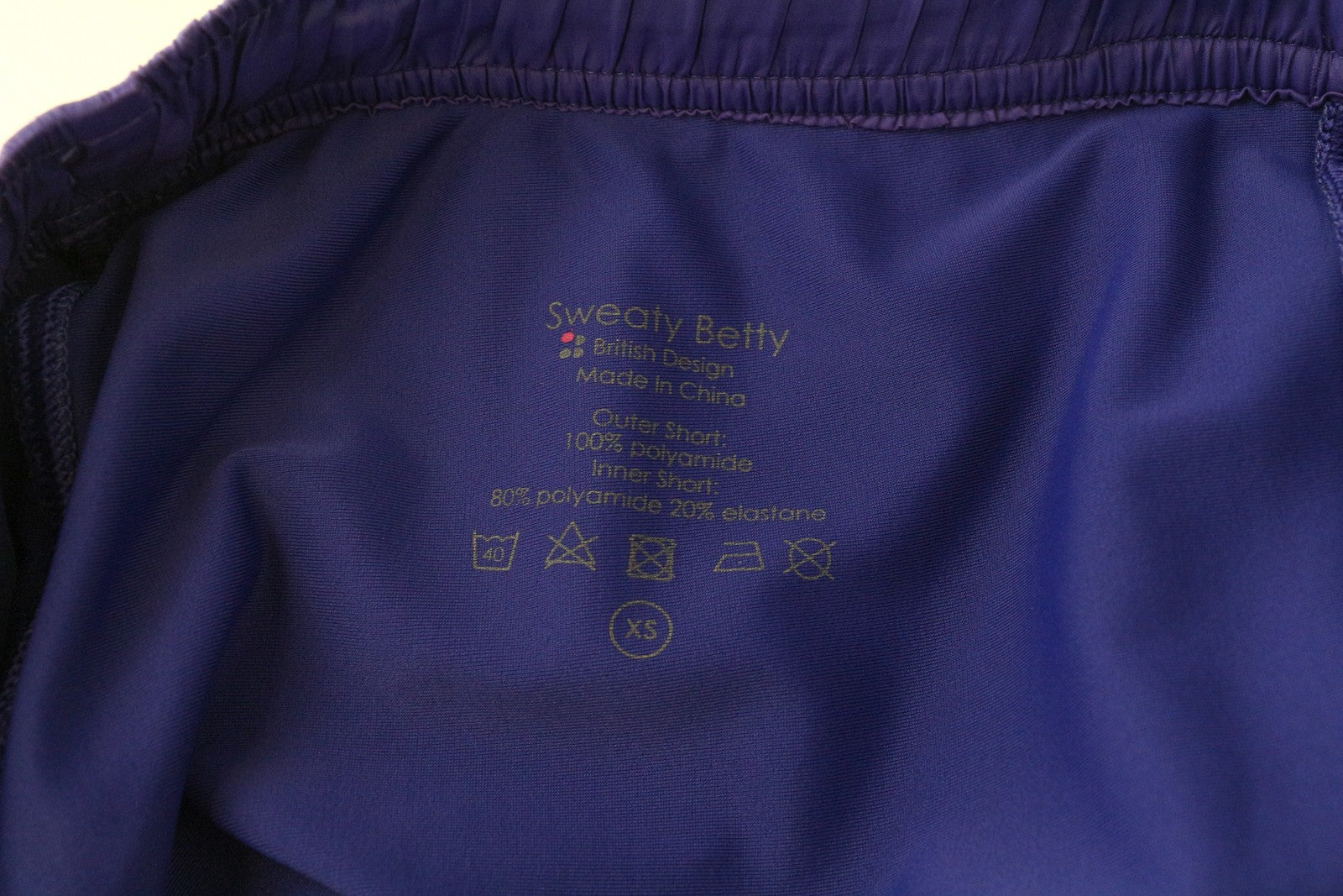 „SWEATY BETTY XS“ violetiniai sportiniai šortai su logotipu. Moteriški daugiasluoksniai sportiniai šortai su užtraukiamu logotipu. 